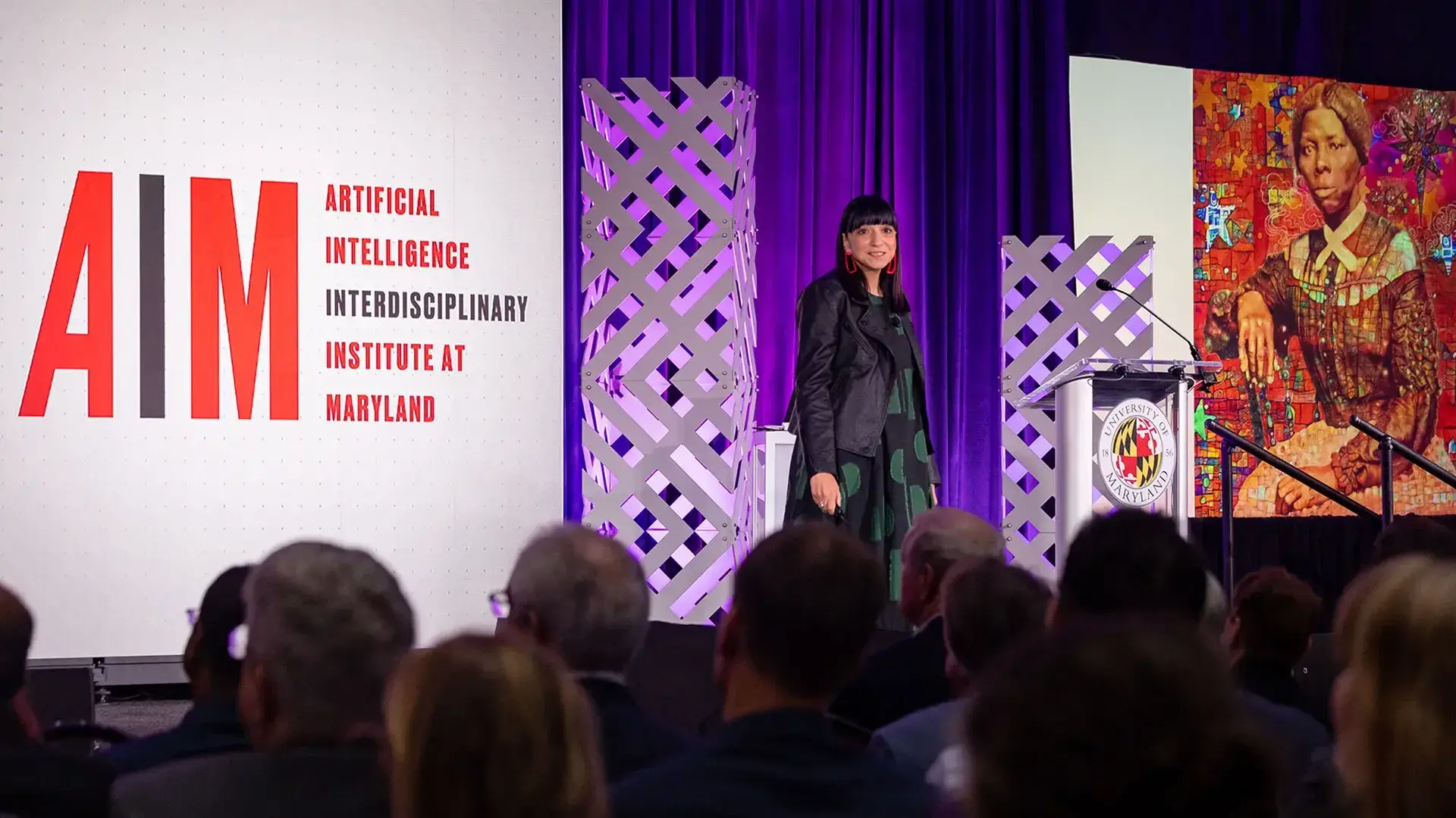Woman standing on a stage with AIM and an art piece on screens