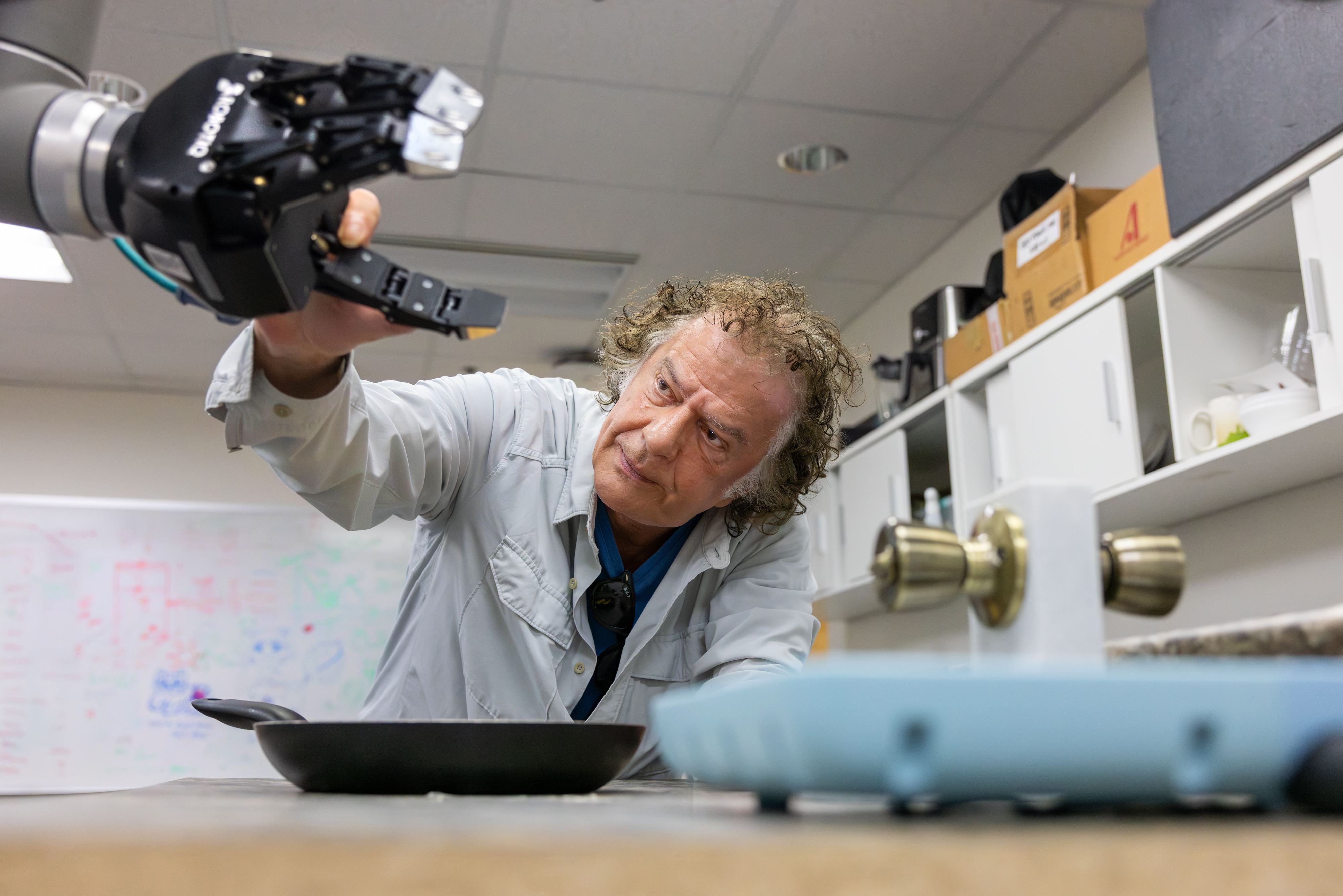 Yiannis Aloimonos tinkering with a robot that learns to cook by watching YouTube videos