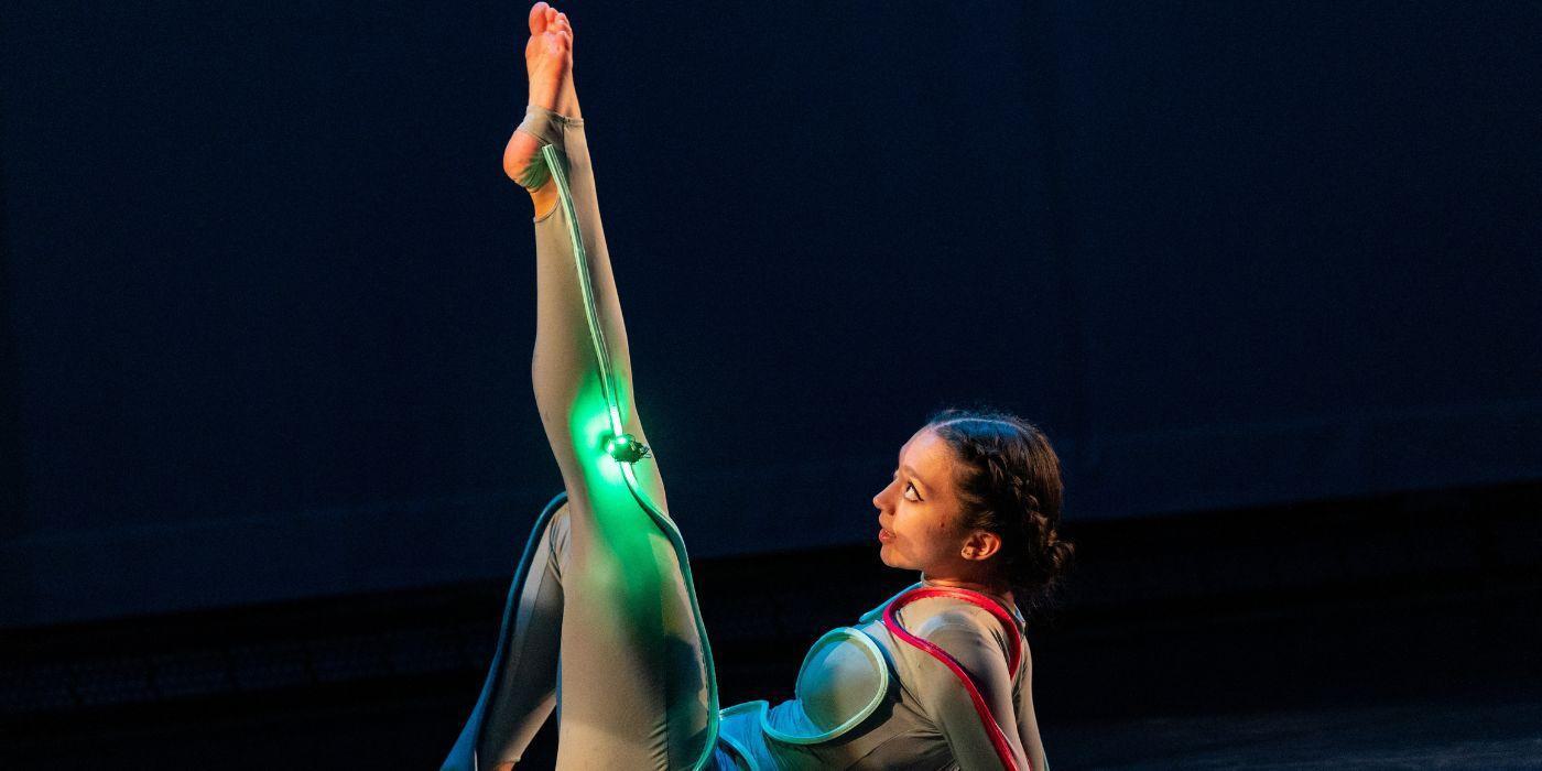 Dancer on stage ground with a leg extended in the air, light cords