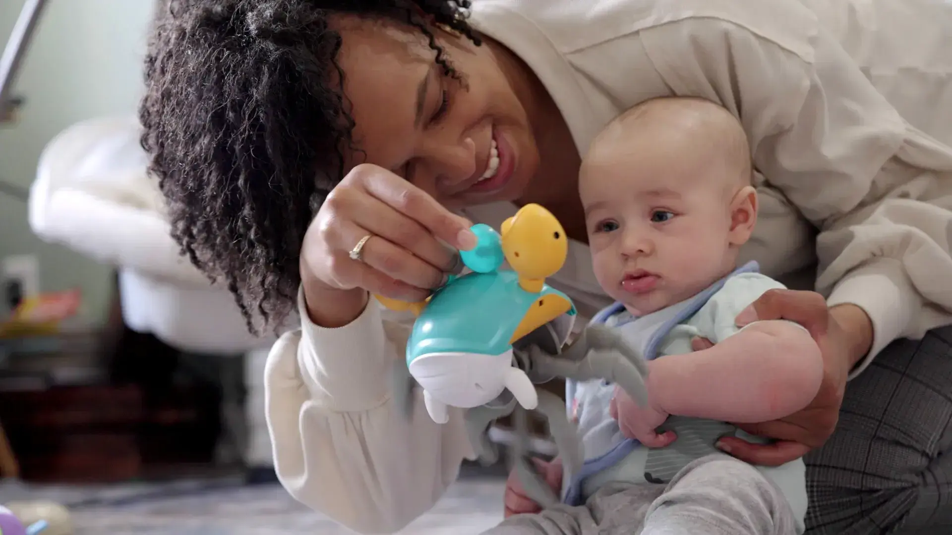 A parent smiles as they hold a toy in front of a young baby