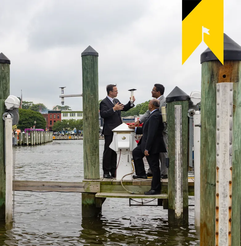 HydroNet researcher Tim Canty stands on a dock in Annapolis and shows a new sensor to University President Darryll J. Pines and Dean of the College of Computer, Mathematical & Natural Sciences Amitabh Varshney