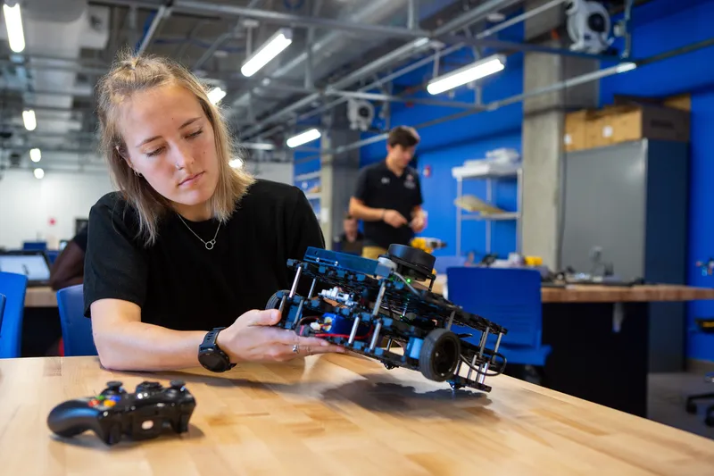 "Madelyne Rossmann, undergraduate Aerospace Engineering student, poses with Turtlebots inside of the Robotics and Autonomy Lab at the IDEA Factory."