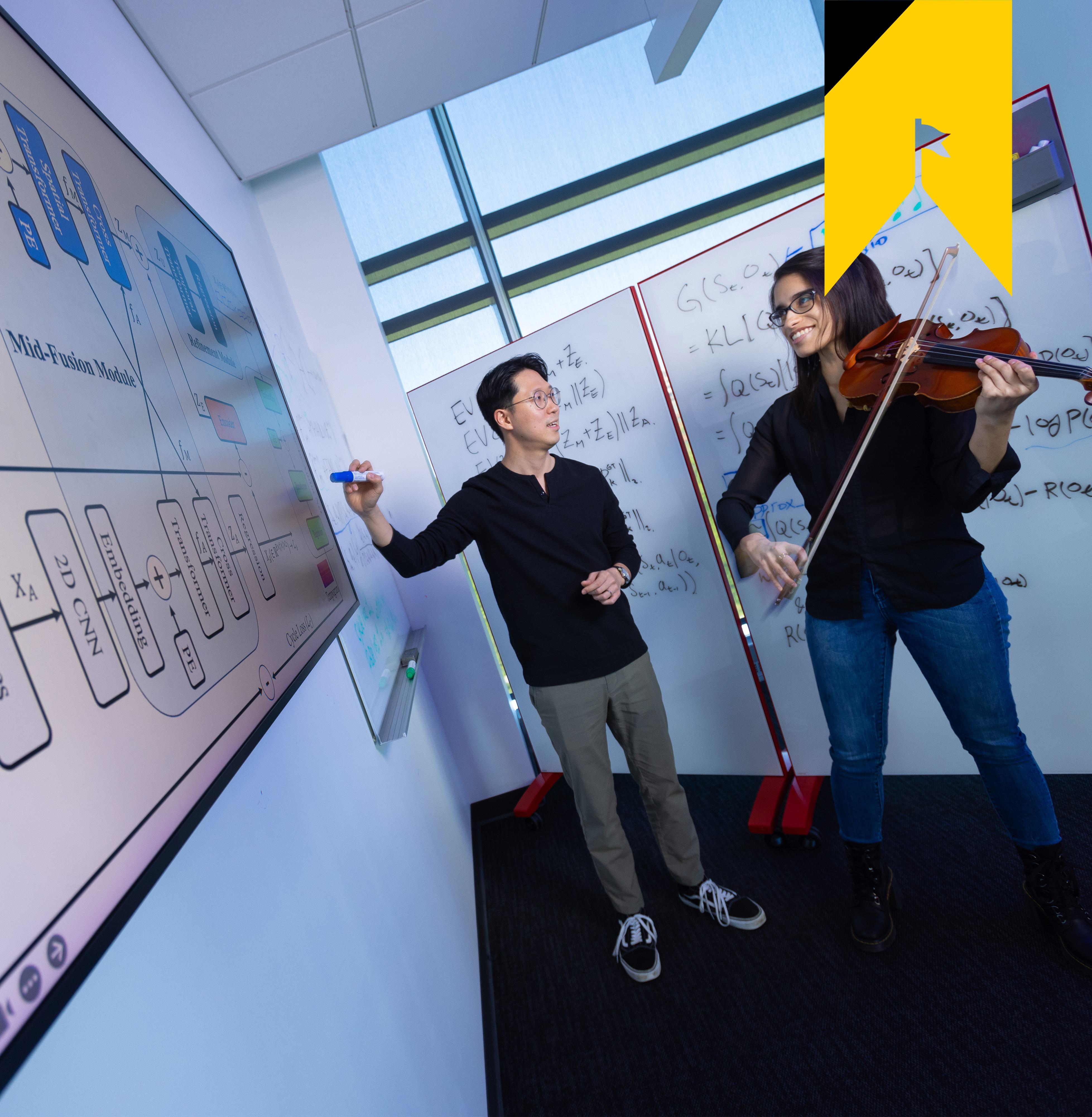 A person playing a violin stands beside a person at a whiteboard