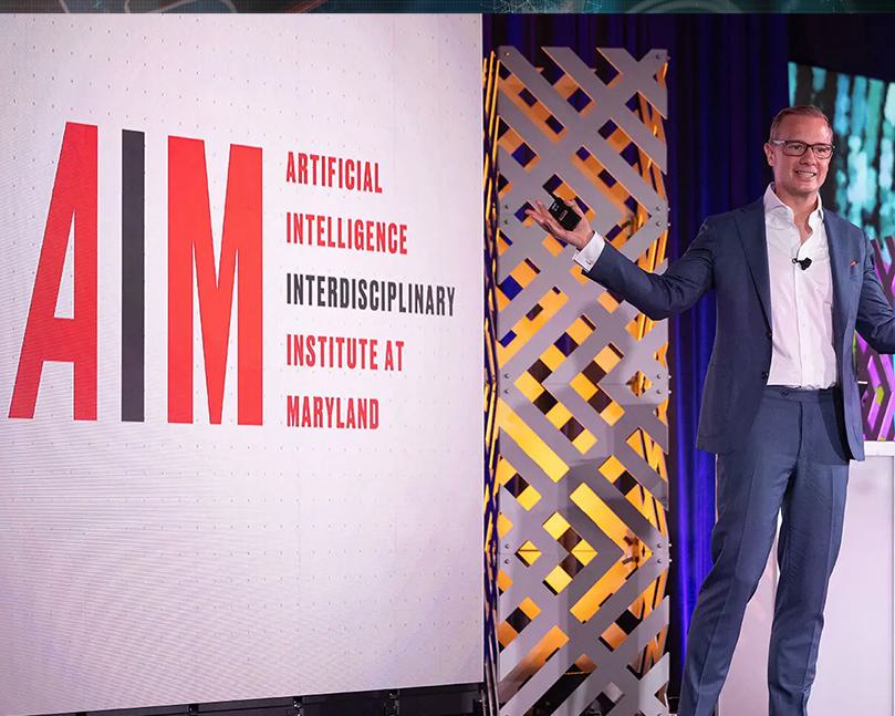 Man giving a presentation on stage in front of a screen with AIM
