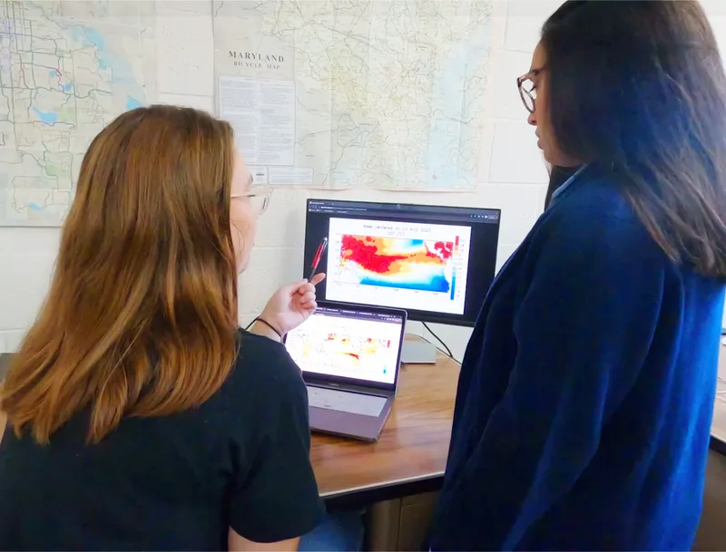 2 students studying a monitor with weather maps