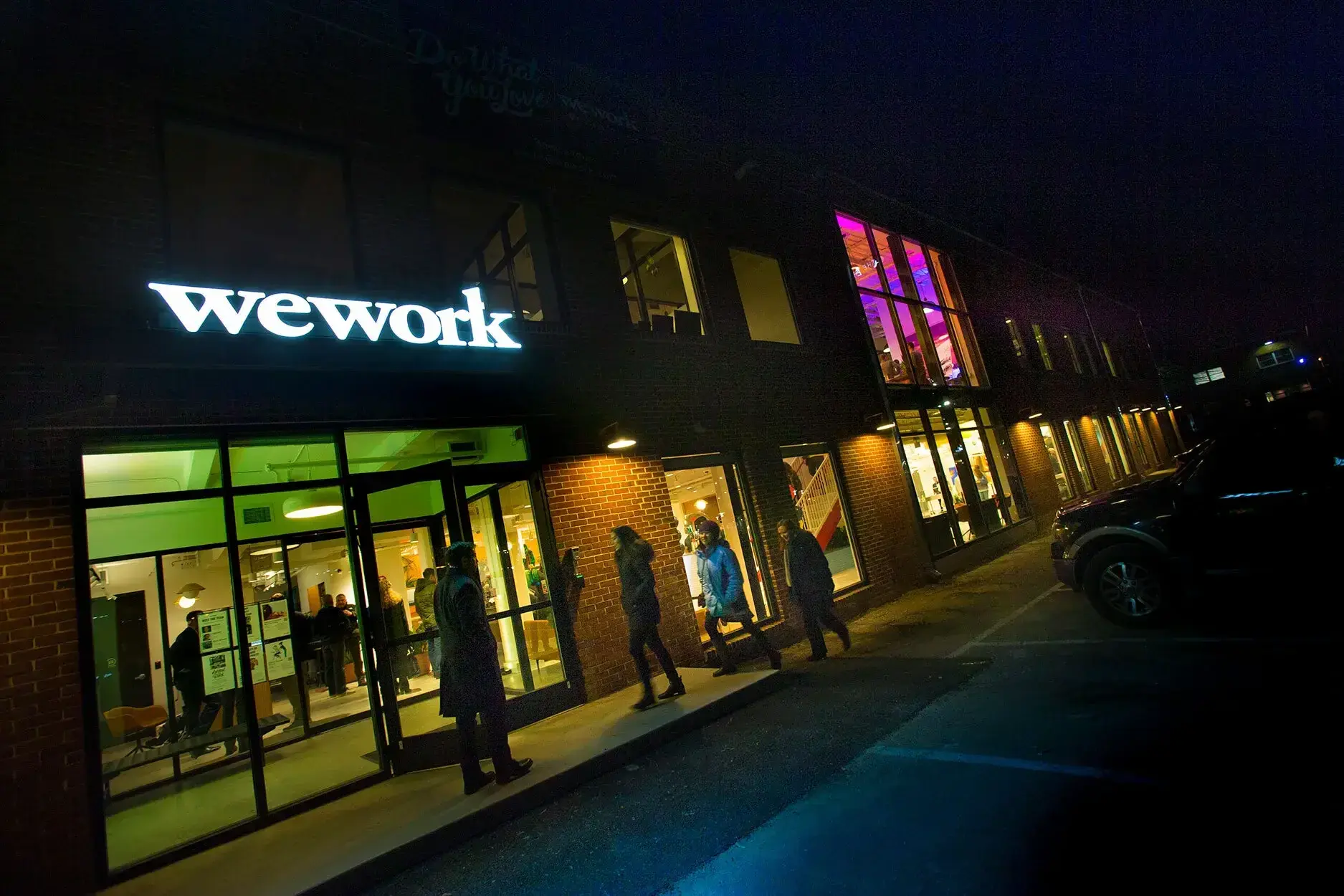 A nighttime view of the WeWork offices near the University of Maryland campus. warm light spills out from the tall windows along the front side of the building.