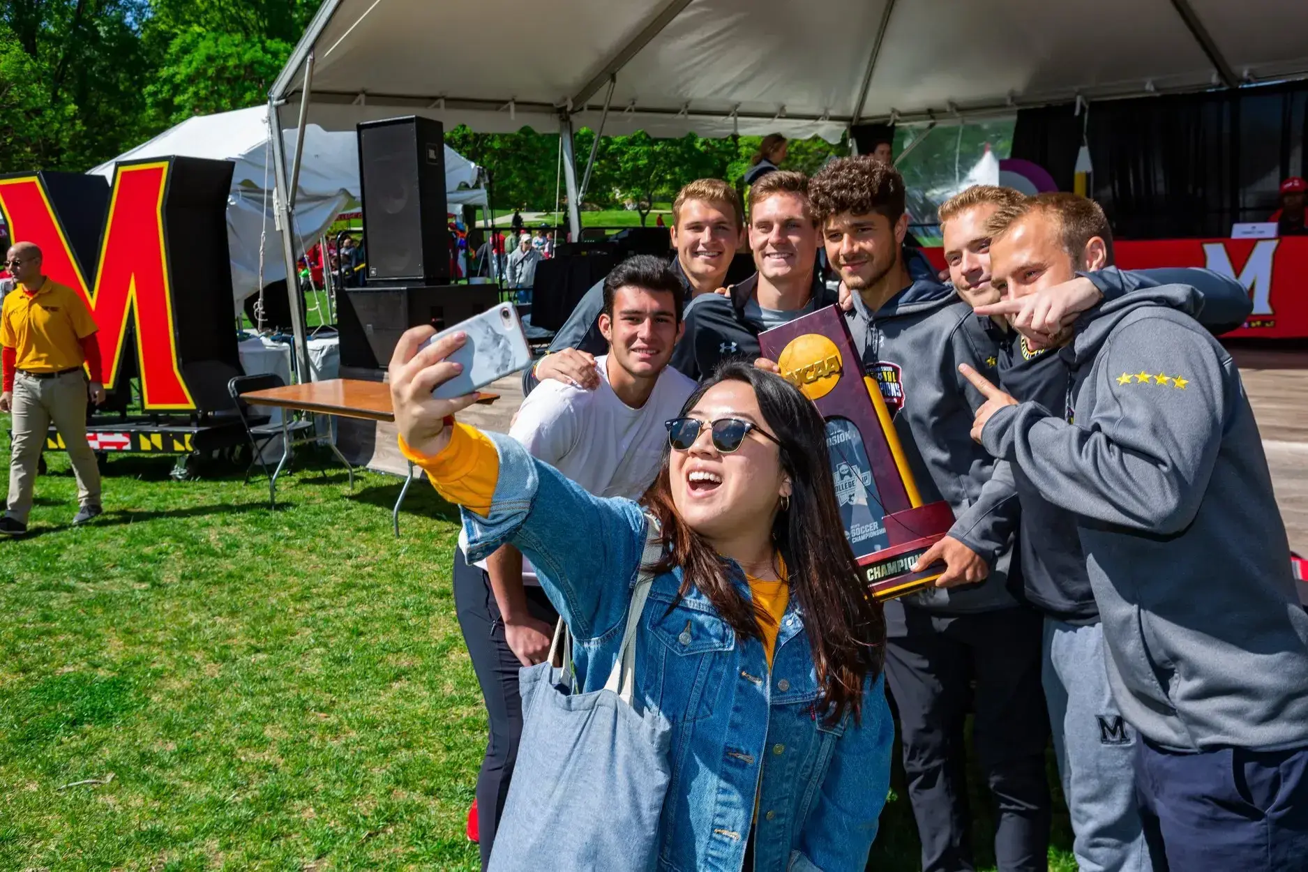 A Maryland Day attendee poses with the University's NCAA Champion team-members holding their trophy