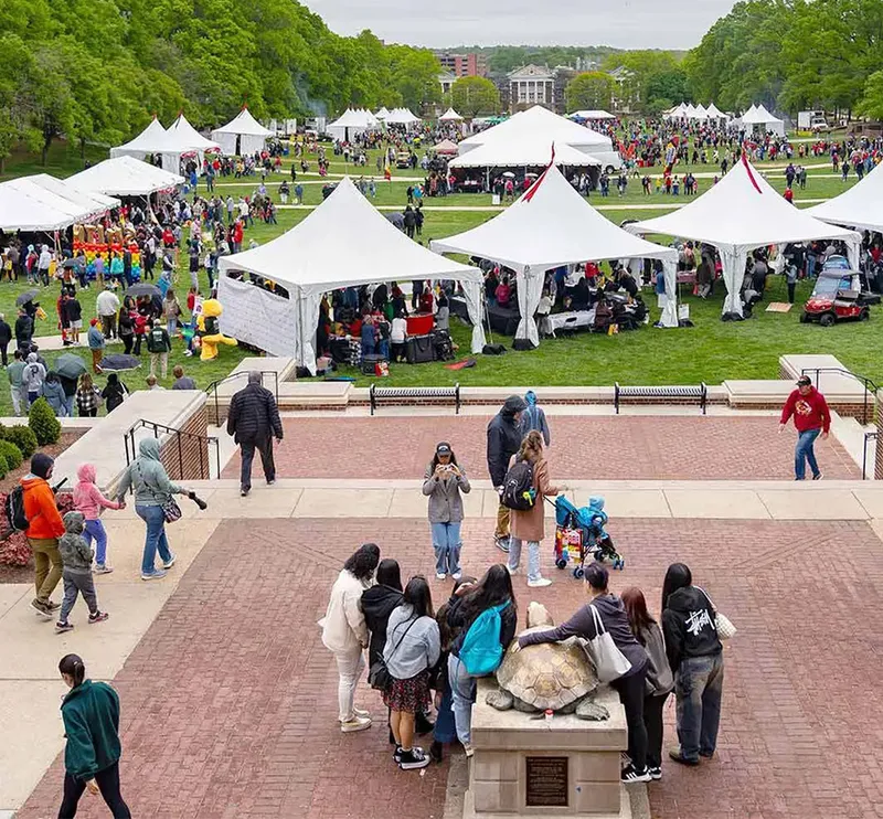 Outdoor green space in front of a traditional building with white tents set up and lots of people.